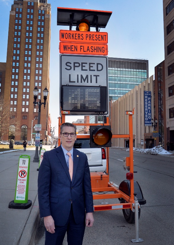 Mark Huizenga standing in front of a construction speed limit sign with a dark blue suit and tie